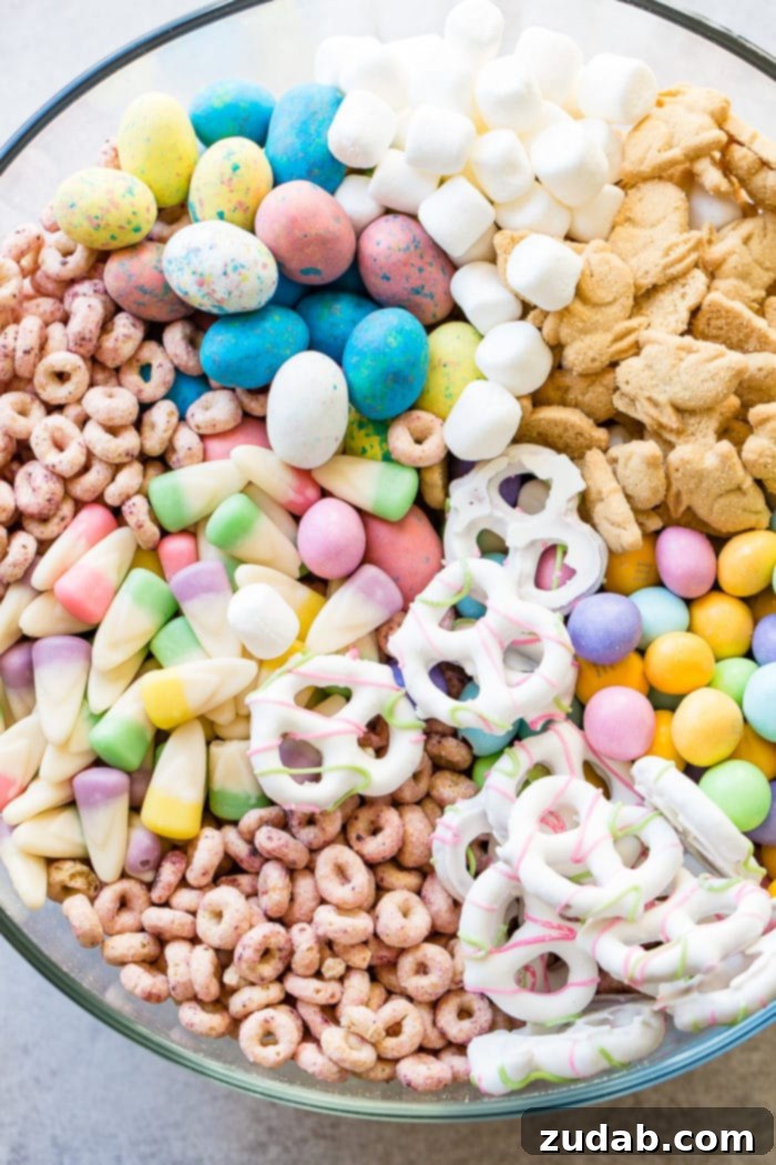 Effortless Easter Snack Medley 2 A vibrant Easter snack mix in a clear glass bowl, featuring berry Cheerios, pastel candy corn, yogurt-covered pretzels, speckled malt Robin eggs, Easter M&Ms, mini marshmallows, and charming bunny cookies, ready for a festive celebration.