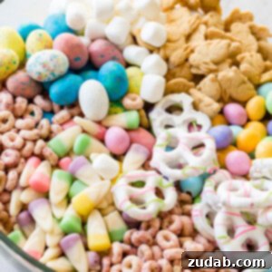 Effortless Easter Snack Medley 7 Easter snack mix in a clear glass bowl with berry Cheerios, Easter candy corns, yogurt covered pretzels, Robin eggs, Easter M&Ms. mini marshmallows and bunny cookies.