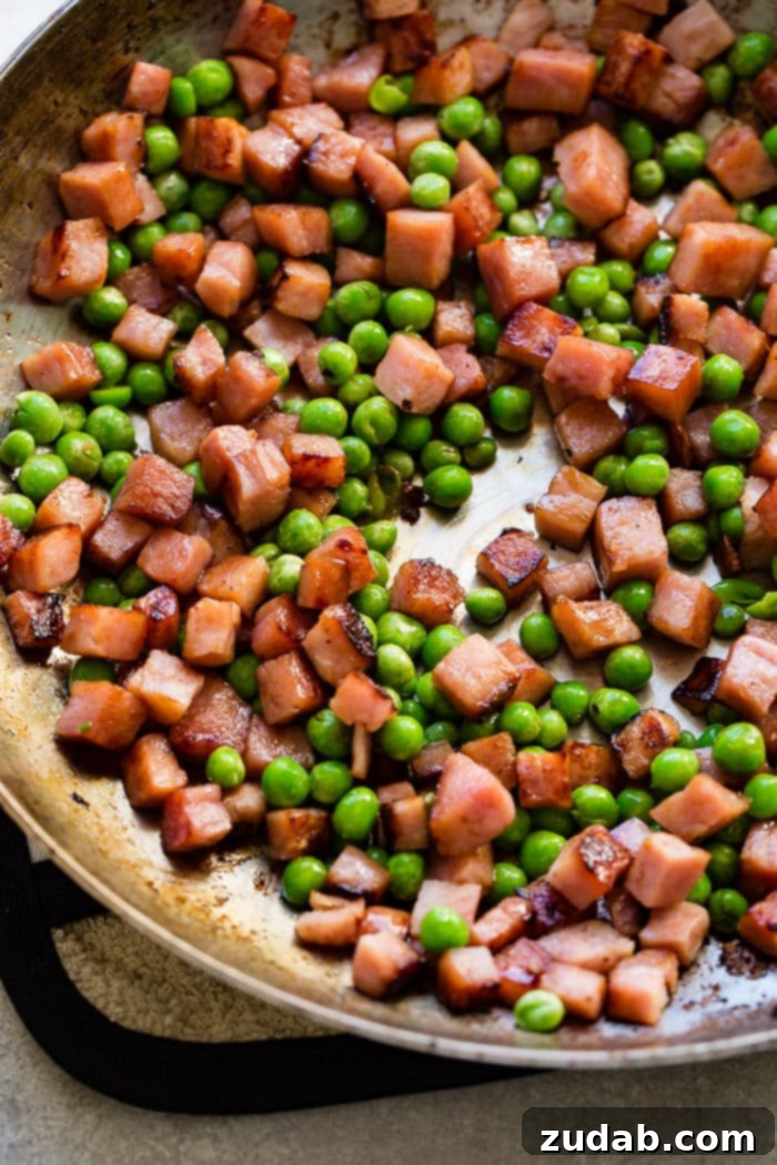 Cubed ham and peas sautéing in a hot skillet, ready for lemon cream pasta.