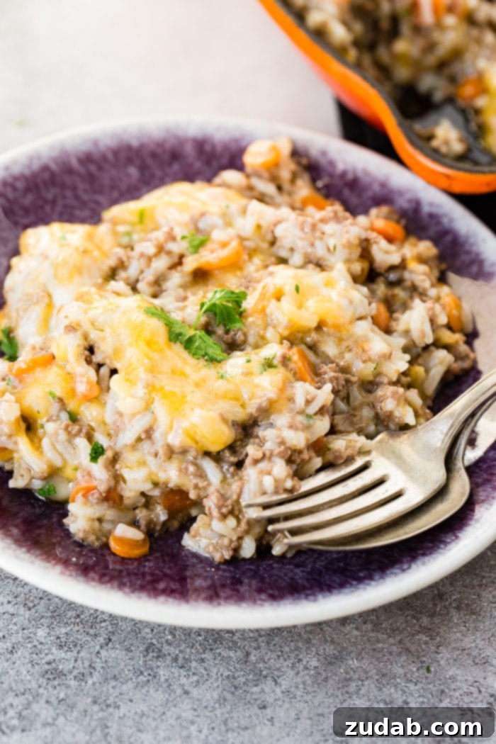 A photo of a serving of cheesy ground beef Instant Pot casserole on a purple plate with a fork and spoon sitting on the side of the plate.