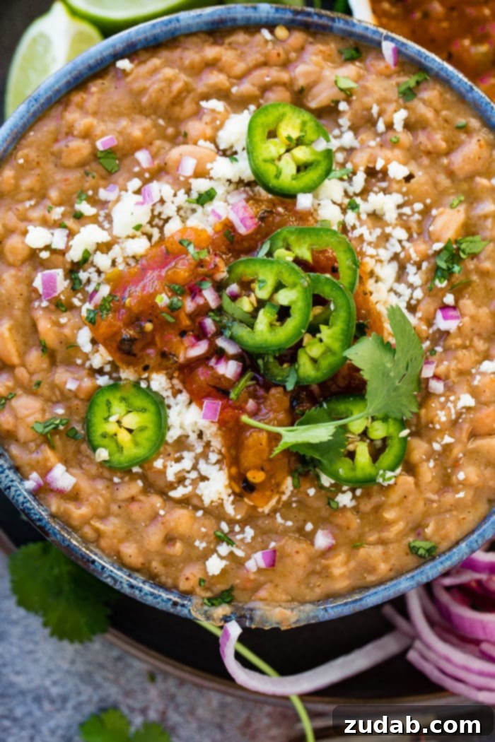 Restaurant-Quality Instant Pot Refried Beans 3 A vibrant close-up of Instant Pot refried beans, garnished with fresh cilantro, lime wedges, diced red onion, and crumbled Cotija cheese. A truly irresistible side dish.