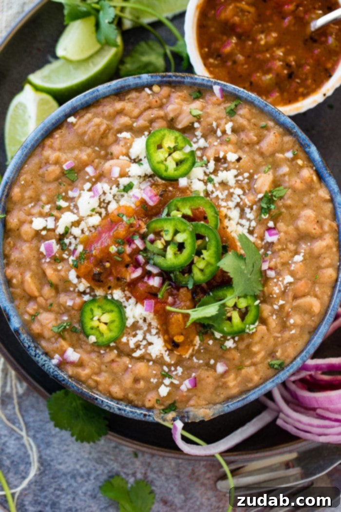 Restaurant-Quality Instant Pot Refried Beans 6 A close-up of a dark blue bowl filled with the best Instant Pot refried beans, garnished with fresh cilantro, sliced jalapenos, and a sprinkle of Cotija cheese. The rich, creamy texture is evident.