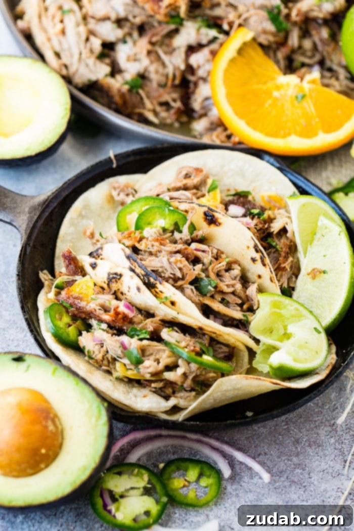 Crispy Tender Pork Carnitas Recipe 5 A photo of three pork carnitas tacos in a cast iron skillet topped with fresh jalapeno slices, diced red onions, and cilantro with a squeezed lime on the side.