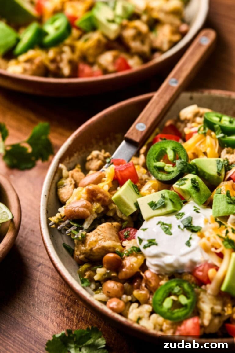 a photo of a chicken burrito bowl in a wooden bowl topped with sliced jalapenos, sour cream, avocado