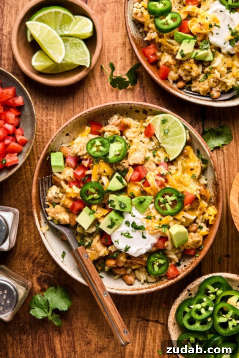 a photo of chicken burrito bowl topped with sliced jalapenos, sour cream, diced tomatoes and chunks of avocado