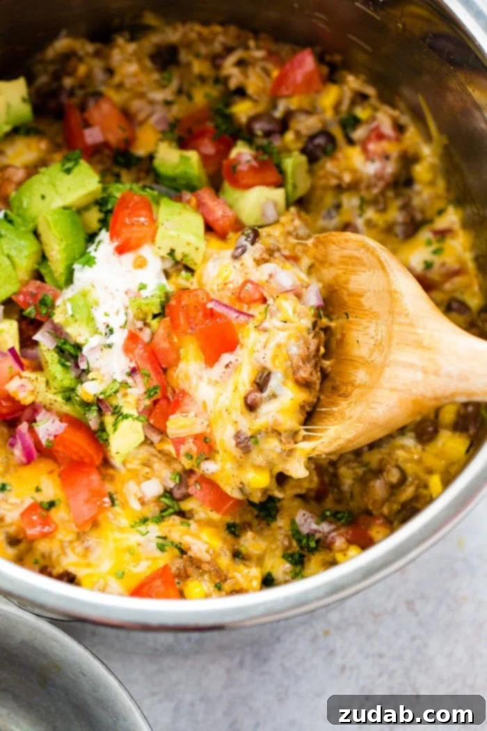 Instant Pot Ground Beef Burrito Bowls in Minutes 4 A photo of instant pot ground beef burrito bowl topped with chopped tomatoes, avocado chunks, and chopped fresh cilantro, with a wooden spoon scooping out a generous portion.