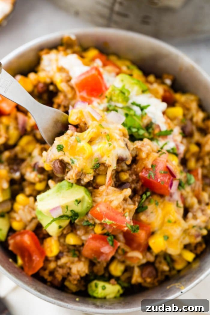 Instant Pot Ground Beef Burrito Bowls in Minutes 5 A close-up photo of an Instant Pot Ground Beef Burrito Bowl, richly textured with beef, rice, and beans, and adorned with fresh toppings. A fork is poised to take a delicious bite.