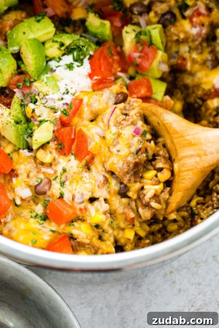 Instant Pot Ground Beef Burrito Bowls in Minutes 7 A photo of an Instant Pot Ground Beef Burrito Bowl, generously topped with fresh tomatoes, avocado chunks, and cilantro, with a wooden spoon scooping out a serving. This image suggests a delicious and easy meal perfect for dinner.