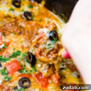 Ultimate Slow Cooker Taco Dip 8 a close up of slow cooker taco dip with a chip scooping some up with olives and fresh cilantro on top