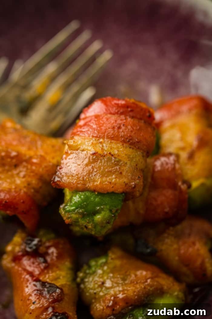 Crispy Bacon Avocado Bites 2 A dark purple plate with a few forks on the left, and a pile of avocado pieces with brown sugar bacon wrapped around them which have been baked and are crispy!