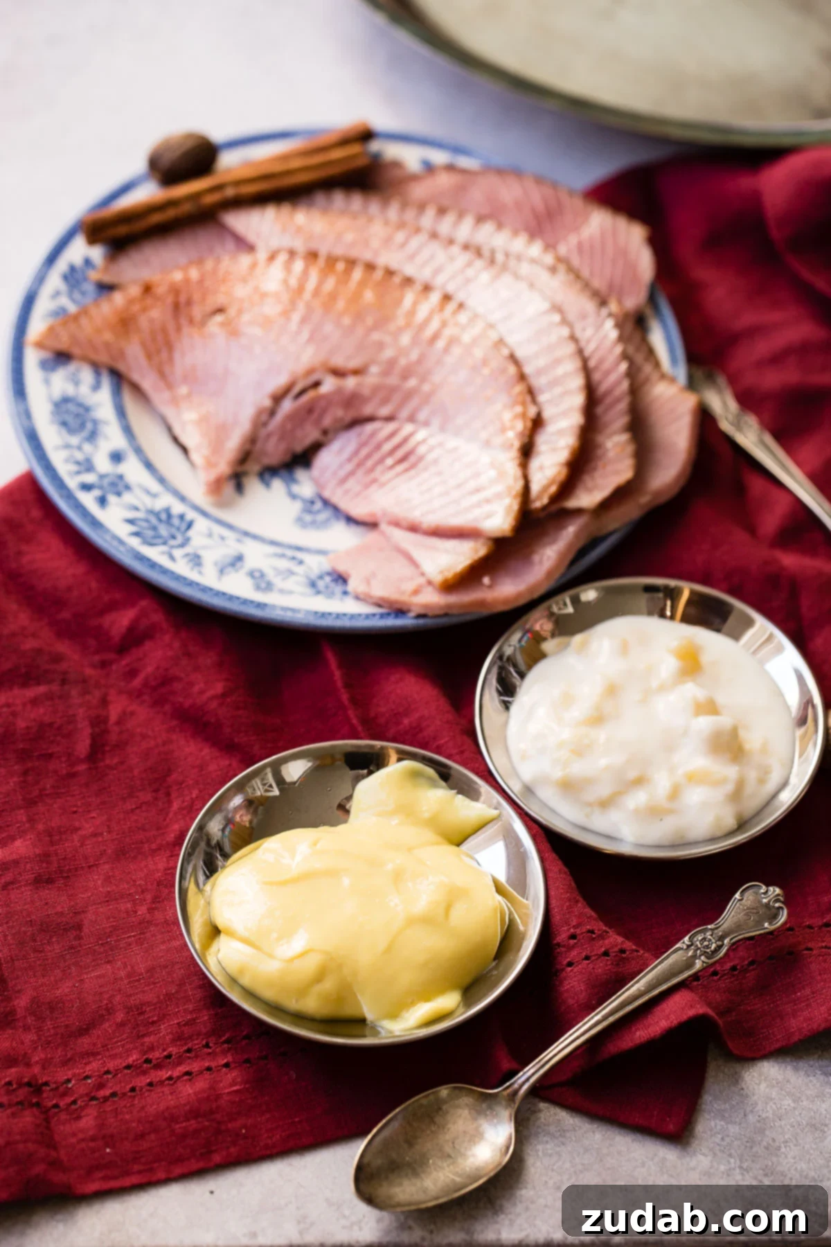 Simple Sauces That Make Ham Shine 2 A beautifully arranged platter of succulent ham slices, with two elegant small bowls showcasing vibrant dipping sauces positioned nearby.