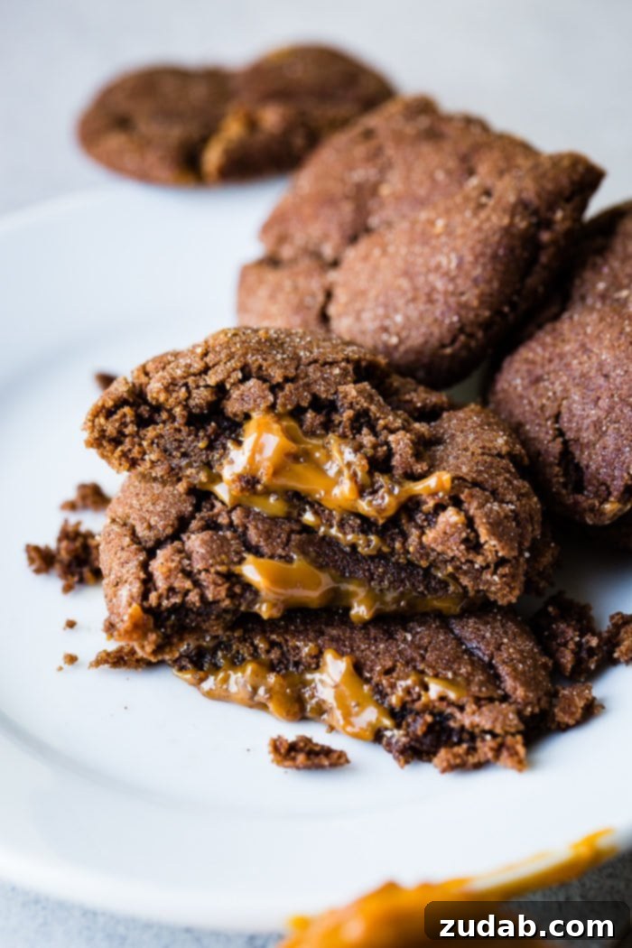Dulce De Leche-Filled Mexican Chocolate Delights 3 A tantalizing close-up of three halved Dulce de Leche Stuffed Chocolate Mexican Cookies, showing the thick, golden caramel oozing from the soft chocolate interior. Whole cookies are artfully piled in the background.