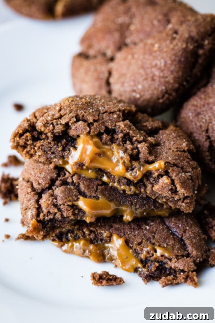 Dulce De Leche-Filled Mexican Chocolate Delights 5 An inviting arrangement of Dulce de Leche Stuffed Chocolate Mexican Cookies. Three are halved and stacked, highlighting their creamy caramel centers, with more whole cookies piled generously in the background.
