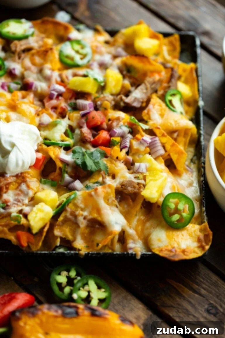 Crockpot Luau Pulled Pork Nachos 3 A close-up shot of a sheet pan filled with golden tortilla chips, topped generously with pulled pork, a cascade of melted cheese, a drizzle of creamy pina colada sauce, finely diced red onions, and fresh chopped cilantro.