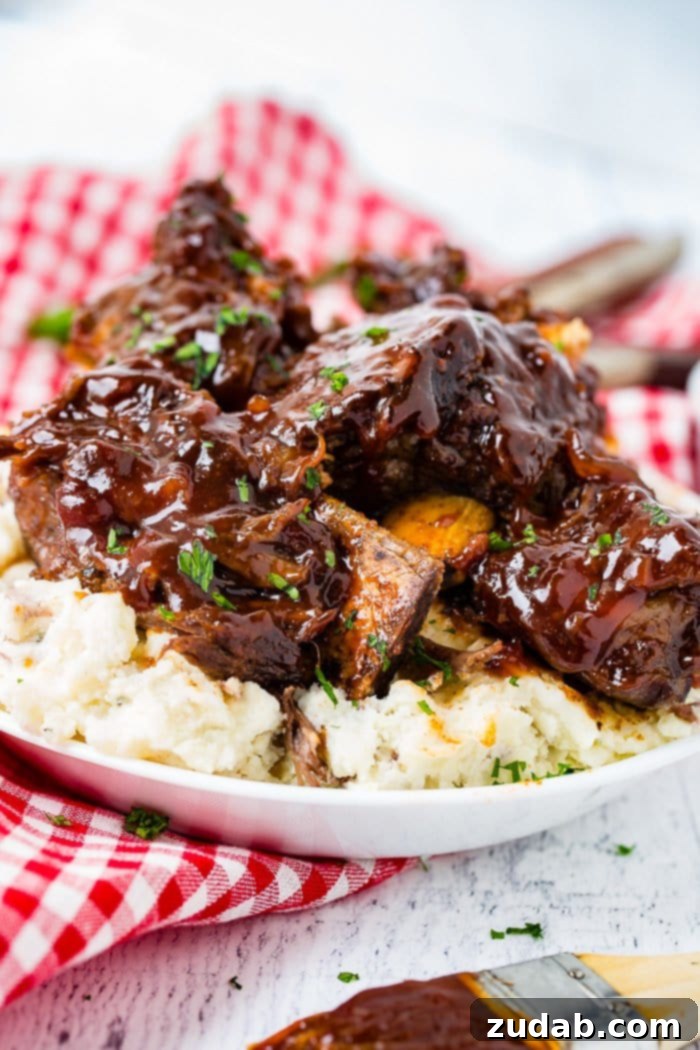 Fall-Off-The-Bone Instant Pot BBQ Short Ribs 2 A photo of sticky bbq beef short ribs piled on top of mashed potatoes on a white plate on top of a red and white checkered cloth napkin.