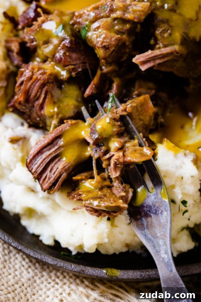 Instant Pot Carolina Gold Beef Short Ribs 5 A photo of beef short ribs smothered in mustard Carolina BBQ sauce over a pile of mashed potatoes with a fork full being taken out.