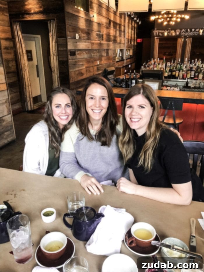 Road Trip Ready Snacks and Entertainment Solutions 12 Three friends are seated at a table in a restaurant, all smiling warmly at the camera. They appear to be enjoying a meal or a social gathering in a relaxed setting.