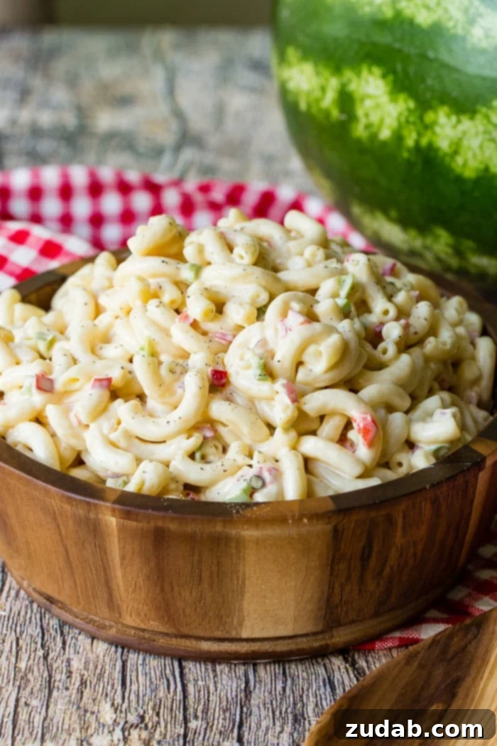 The Ultimate Macaroni Pasta Salad Recipe 3 A wooden bowl on a red and white checkered napkin full of creamy macaroni salad.