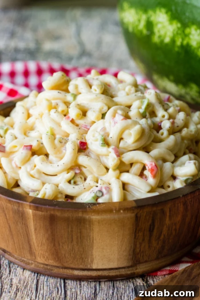 The Ultimate Macaroni Pasta Salad Recipe 6 A wooden bowl with a red and white checkered napkin in the background full of creamy pasta and veggies.