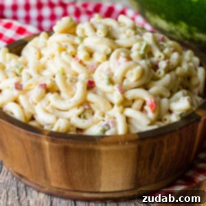 A wooden bowl on a red and white checkered napkin full of creamy macaroni salad.