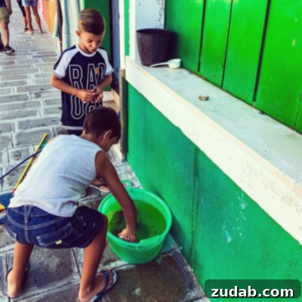 A photo of two boys playing with a bucket full of water and crabs on a stone ledge in Burano, Italy.