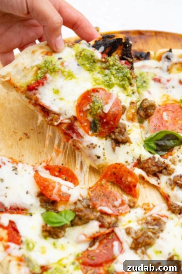 Pesto Pepperoni Grilled Pizza - Oh Sweet Basil A photo of a piece of pesto pepperoni grilled pizza being pulled away from the whole pizza.