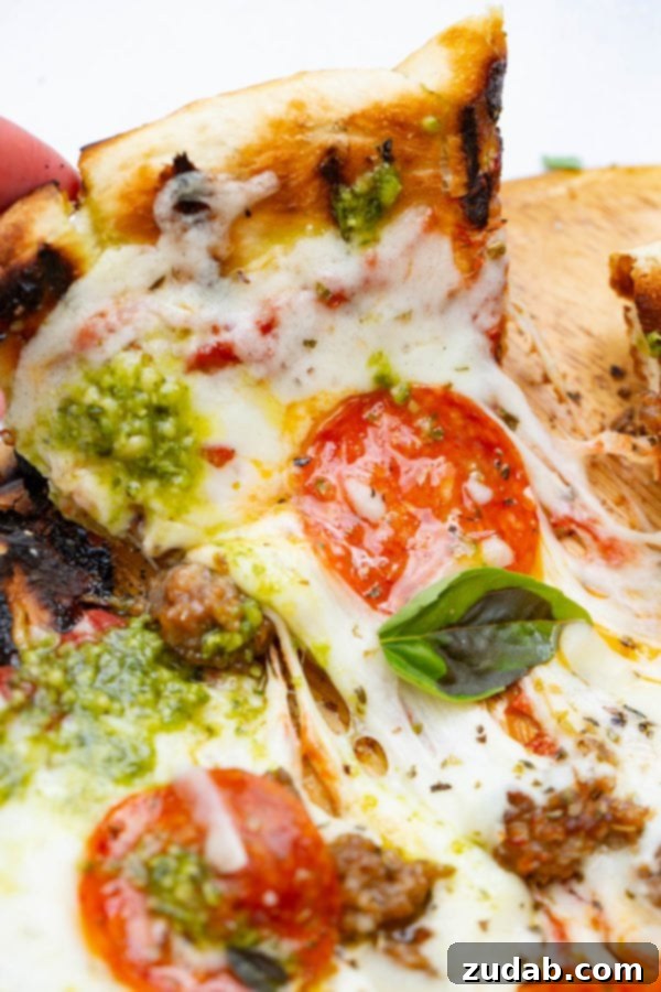 Pesto Pepperoni Grilled Pizza - Oh Sweet Basil A photo of a piece of pesto pepperoni grilled pizza being pulled away from the whole pizza.