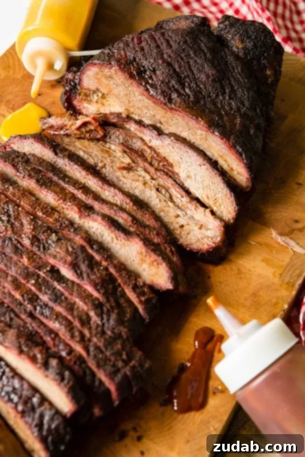 Perfect Smoked Brisket Recipe A photo of perfectly smoked brisket sliced and sitting on a wooden cutting board with bottles of BBQ sauce laying next to it.