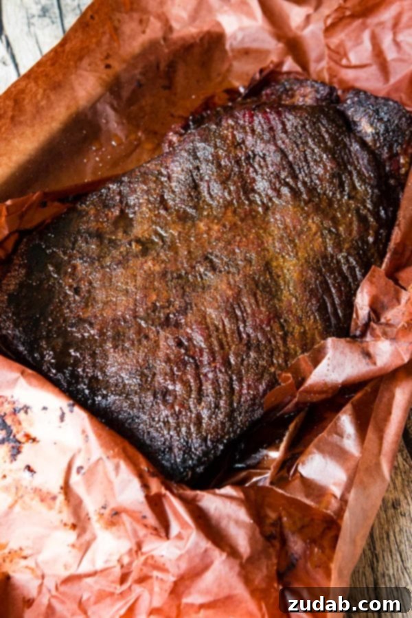Perfectly Smoked Brisket Recipe A photo of a perfectly smoked brisket with a delicious crusty bark sitting in peach butcher paper.