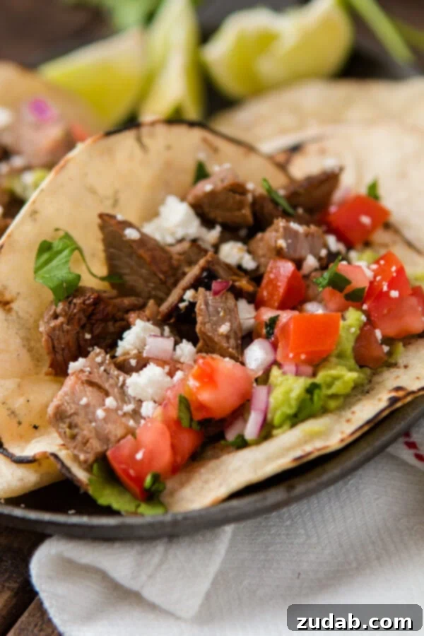 Delicious authentic carne asada taco in a warm corn tortilla with guacamole, red onions and tomatoes on a plate.