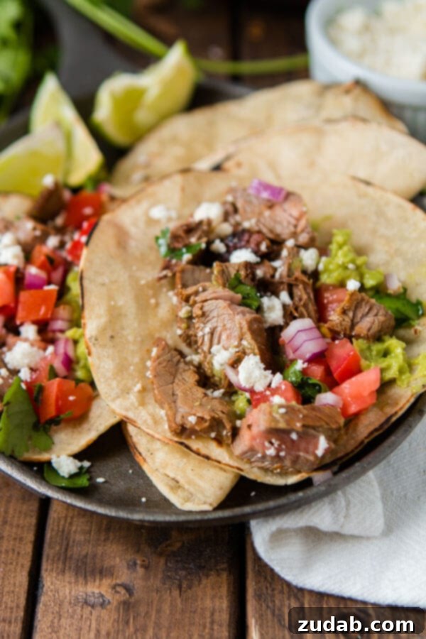 Two delicious authentic carne asada tacos with mexican cheese, onions, steak, cilantro and guacamole on a serving plate on top of a wooden table.