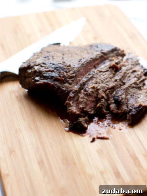 Marinated flank steak sliced with a sliver knife on a wooden cutting board.