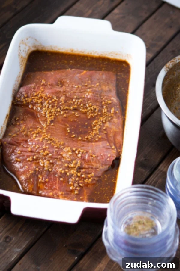 Marinated flank stake in a white casserole dish on top of a wooden table.