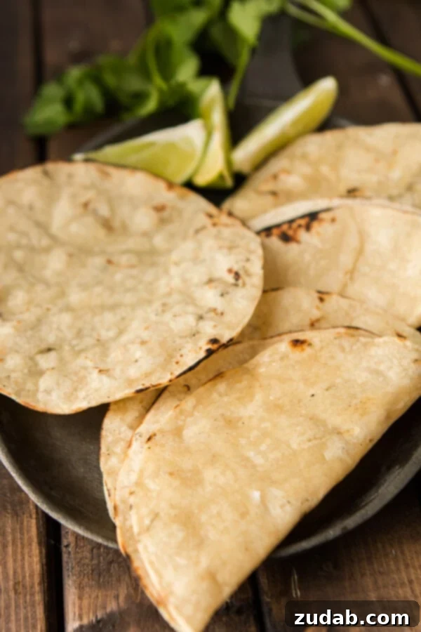 Four freshly charred tortillas on a serving plate on top of a wooden table. 