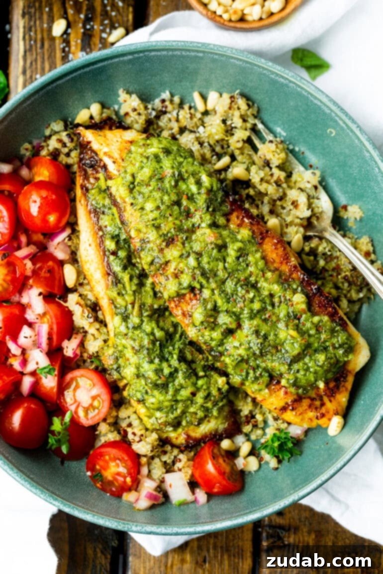 Pesto Tilapia Easy Low Calorie Dinner Video 2 a photo of two golden tilapia filets topped with bright pesto sauce on a bed of quinoa with grape tomatoes on the side