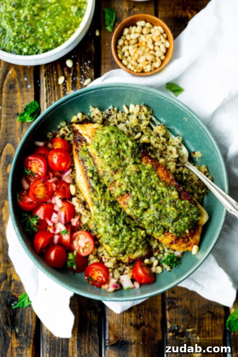 Pesto Tilapia Easy Low Calorie Dinner Video 4 a photo of two golden tilapia filets topped with pesto and sitting on a bed of quinoa with a side of cherry tomatoes