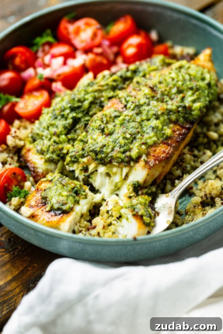 Pesto Tilapia Easy Low Calorie Dinner Video 5 a photo of a fork flaking off a bite of tender tilapia covered with pesto sauce on top of tri colored quinoa.
