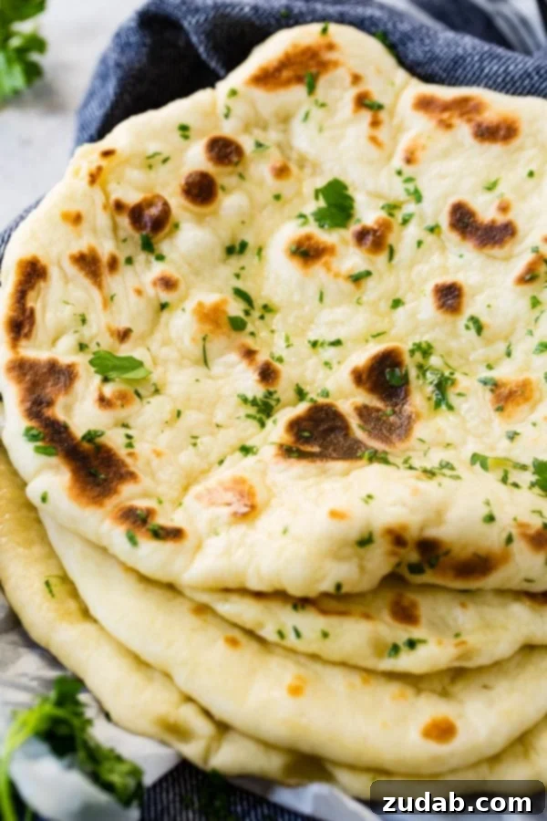 Easy Homemade Naan Recipe A stack of four warm, golden-brown pieces of homemade naan, ready to be served.