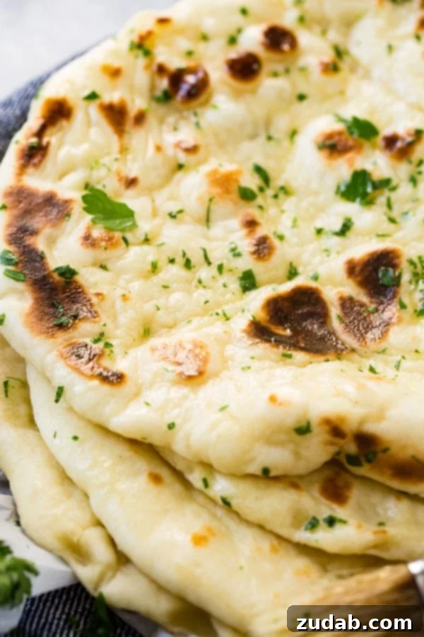 Easy Homemade Naan Recipe Four pieces of warm homemade naan, perfectly stacked, showing off their golden-brown char and tender interior.