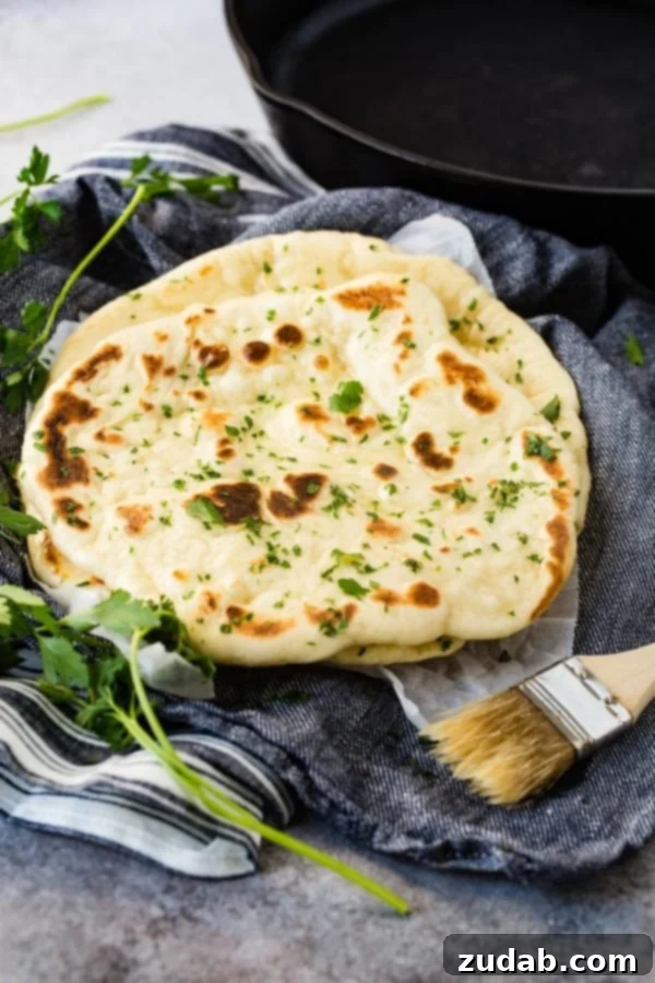 Easy Homemade Naan Recipe Two pieces of golden-brown naan bread resting on a blue cloth napkin, with a basting brush nearby.