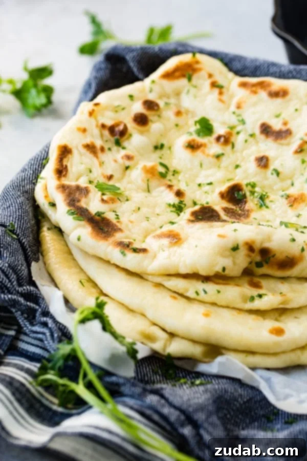Easy Homemade Naan Recipe Four pieces of homemade naan stacked on each other, invitingly warm and ready to be enjoyed.