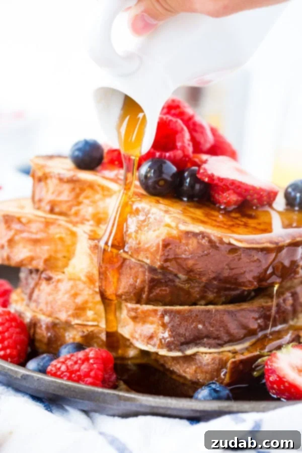 How to Make French Toast A photo of syrup being poured over a stack of french toast covered in fresh berries.