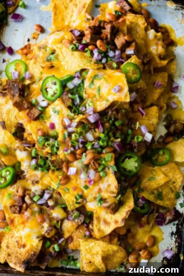 A photo of bbq brisket nachos with melted cheese all over the top and sliced jalapenos, diced red onion and fresh chopped cilantro.