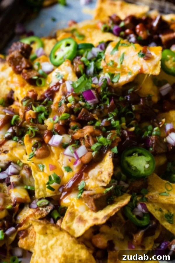 A photo of bbq brisket nachos with melted cheese all over the top and sliced jalapenos, diced red onion and fresh chopped cilantro.