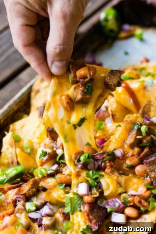 A photo of someone pulling out one cheesy nacho chip from a pile of brisket nachos.
