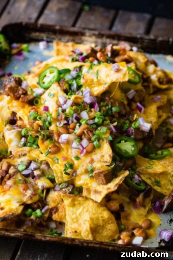 A photo of bbq brisket nachos with melted cheese all over the top and sliced jalapenos, diced red onion and fresh chopped cilantro.