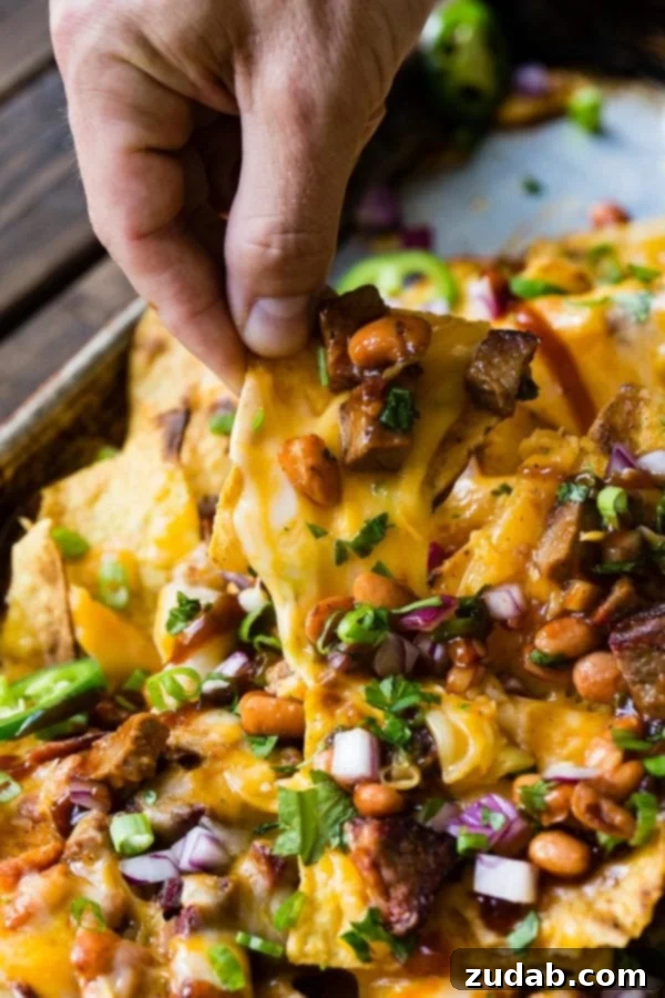 A photo of someone pulling out one cheesy nacho chip from a pile of brisket nachos.