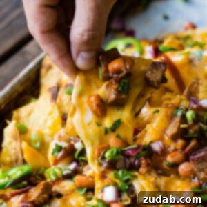 a pile of chips loaded with bbq brisket, beans, gooey cheese and all sorts of extras like jalapenos, red onions and cilantro!