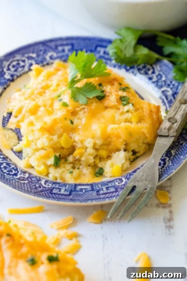 Cheesy Jiffy Cornbread Casserole A photo of a serving of cornbread casserole on a blue and white plate with a fork laying next to the casserole.