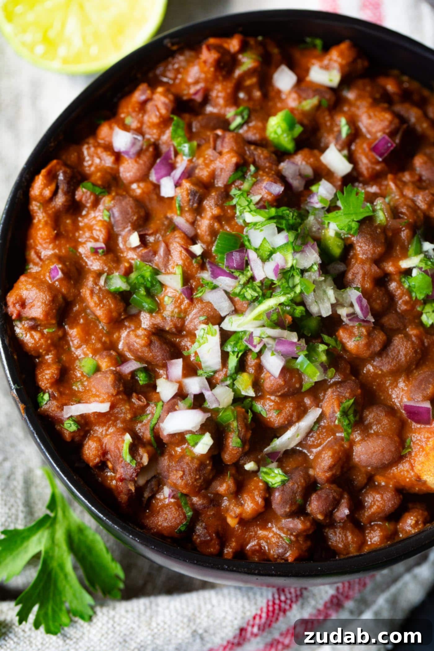 The Most Delicious Mexican Black Beans Ever A vibrant bowl of Mexican black beans topped with finely diced red onion and a generous sprinkle of fresh chopped cilantro, ready to be served.